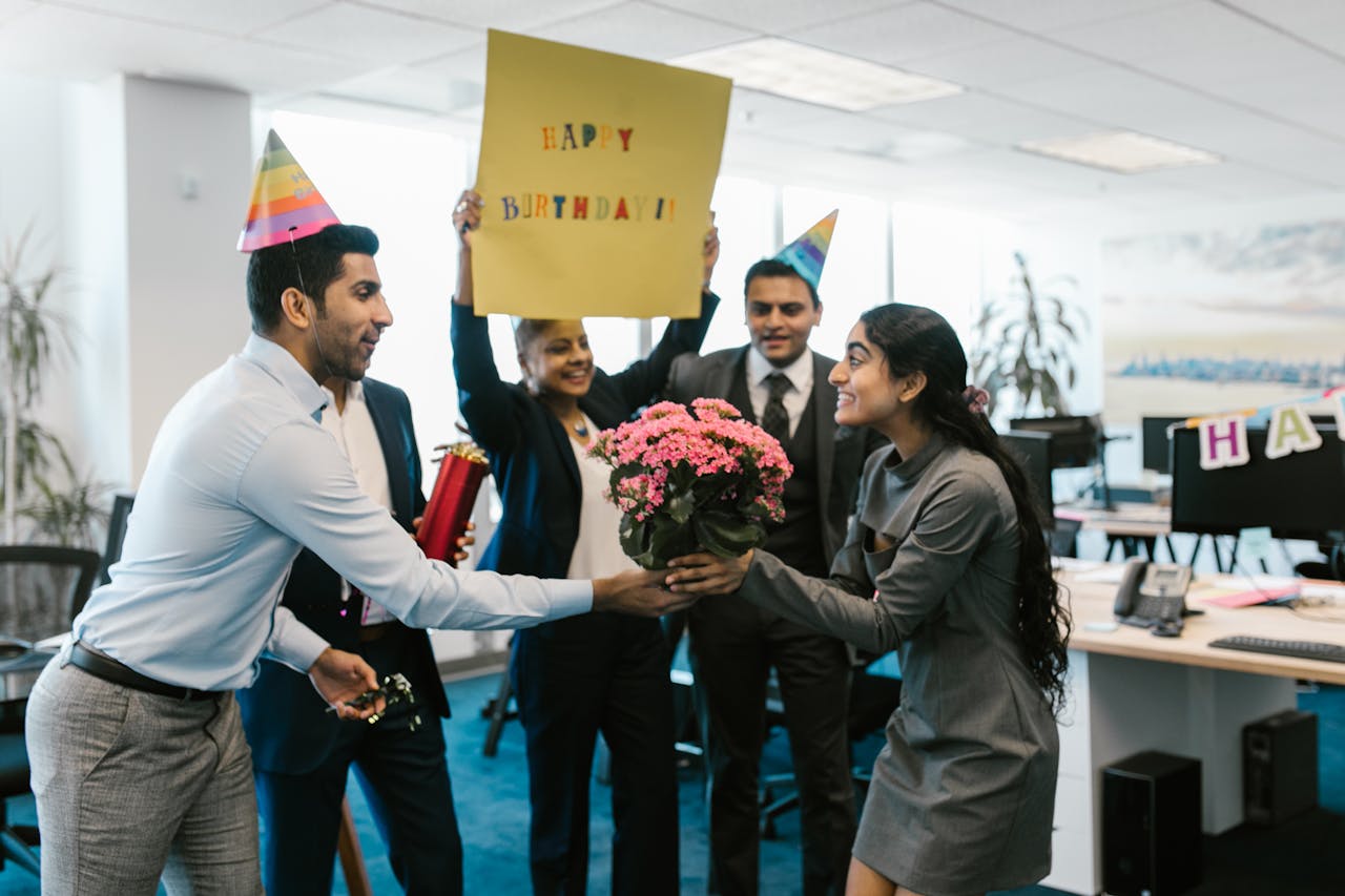 Services Happy office birthday celebration with colleagues exchanging gifts and wearing party hats.